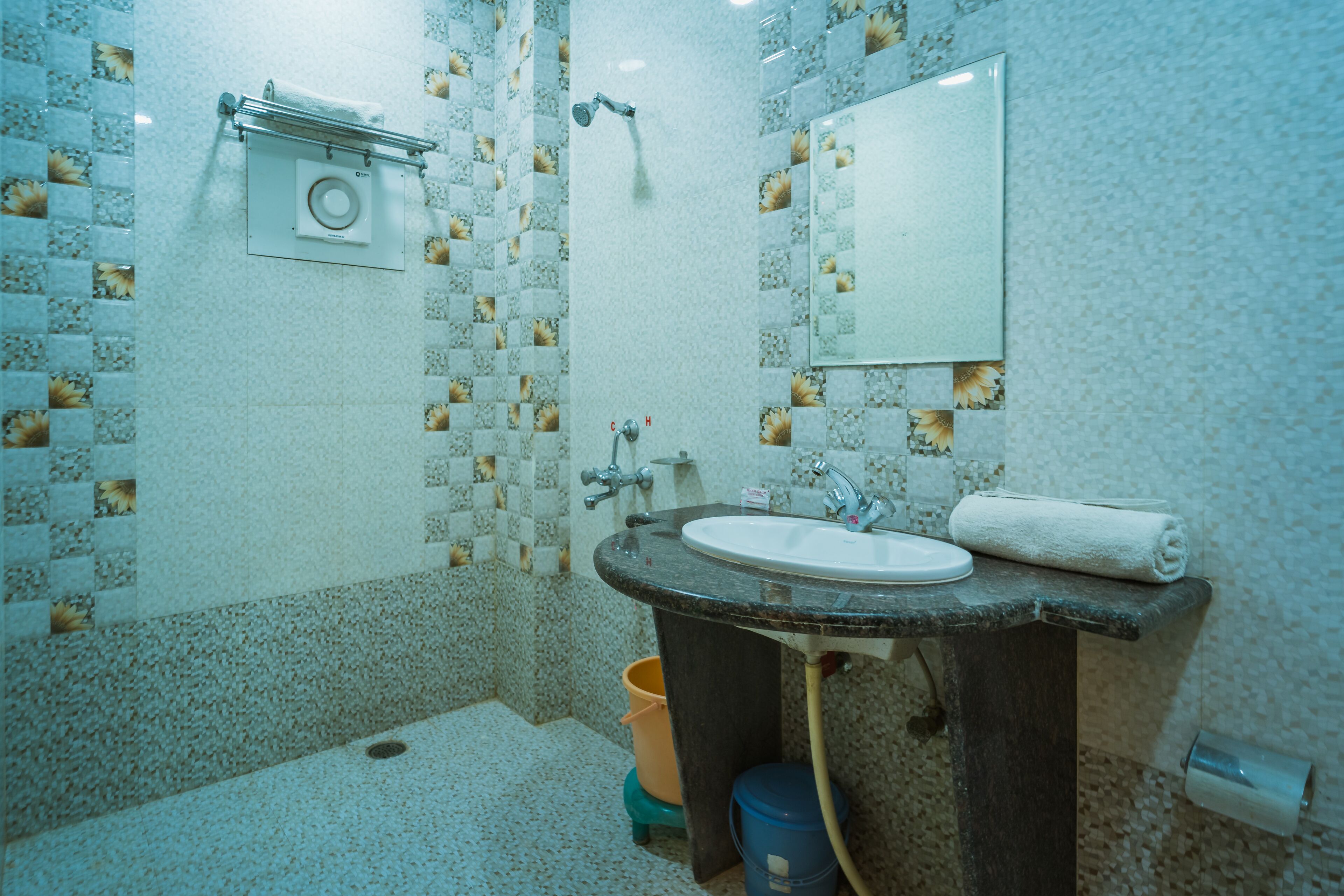 Un bany amb un lavabo, mirall, tendidor de tovalloles, dutxa i rajoles decoratives.