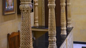 Un intérieur architectural somptueux, orné de sculptures détaillées sur les colonnes et les arcs, avec une œuvre d’art encadrée au mur et un motif de carreaux sur le sol.