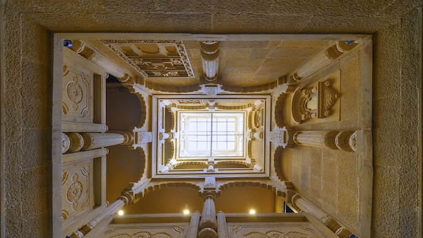Une vue architecturale détaillée d’un vaste hall orné de colonnes richement décorées et doté d’une fenêtre centrale.