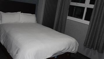 Uma cama em quarto com janela e cortinas.