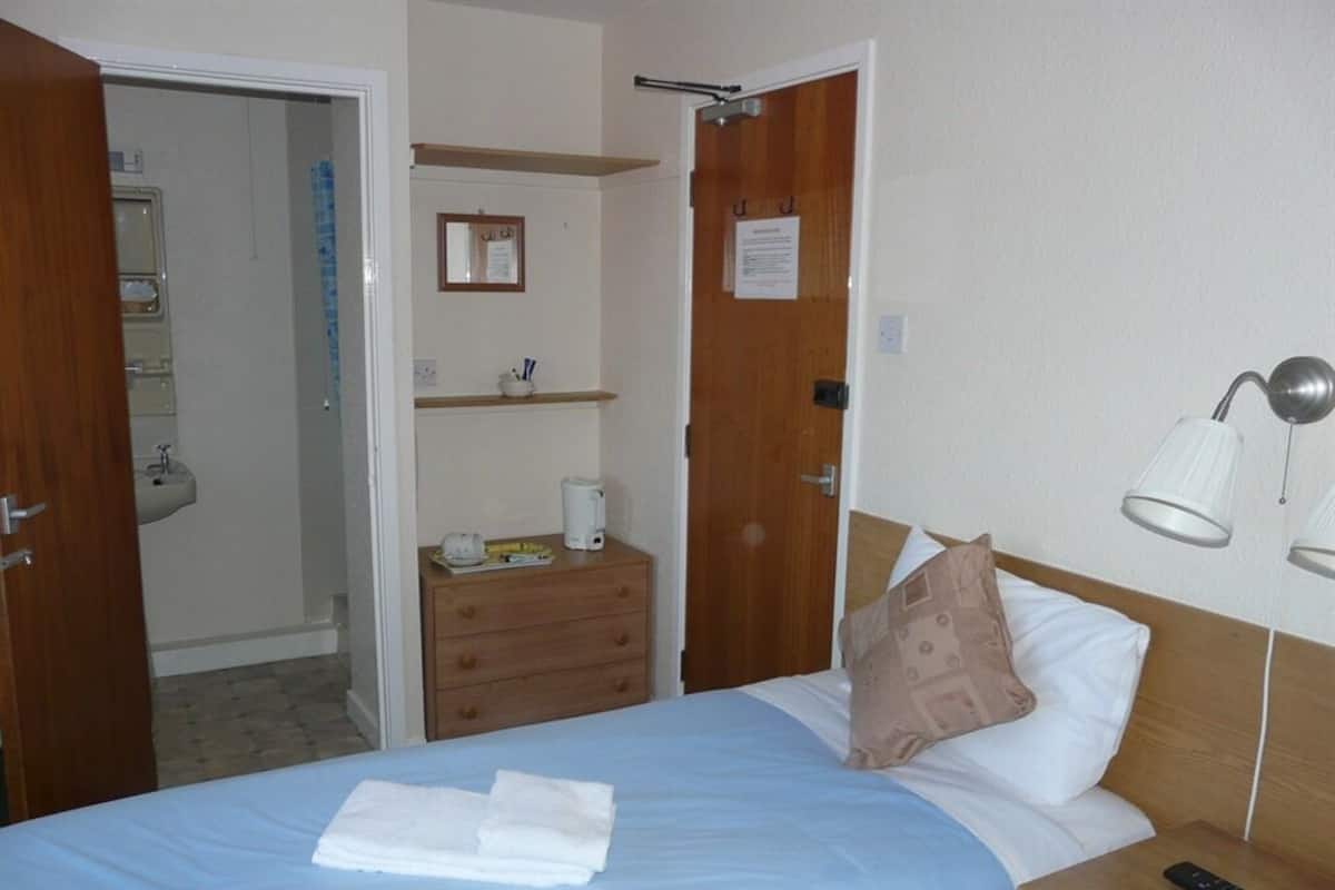 A hotel room with a bed, bedside table, lamp, and a door leading to a bathroom.