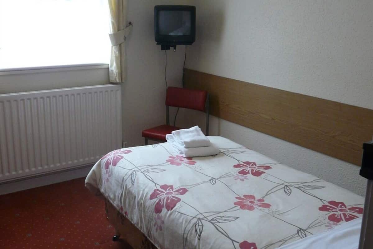 A hotel room with a bed, a red chair, a television mounted on the wall, and a window with curtains.