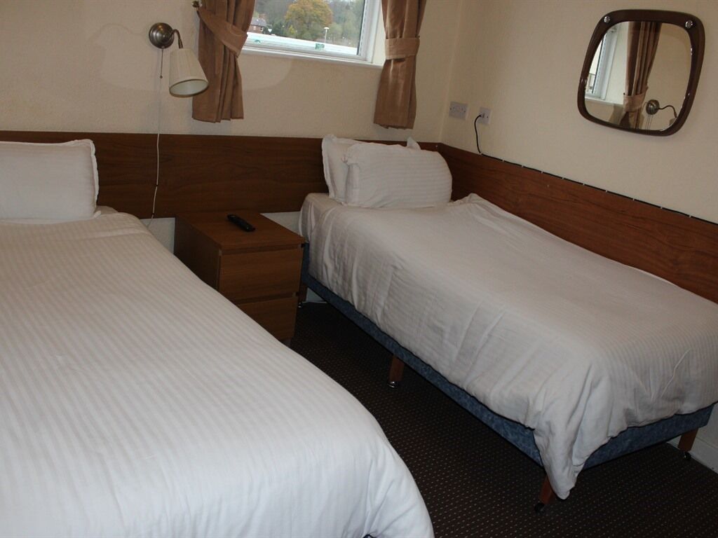 A room with two single beds, a bedside table with a lamp, a mirror, and a window with curtains.