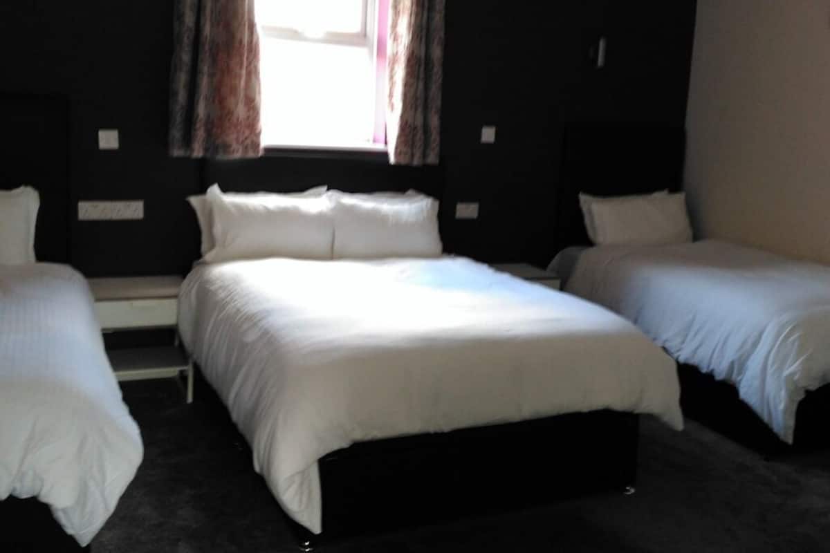 A room with a large bed, two smaller beds, and a window with curtains.