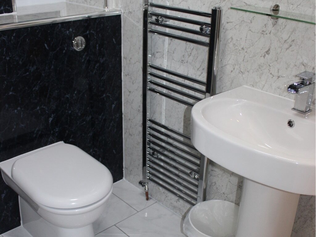 Un baño con inodoro blanco, cabina de ducha de vidrio, toallero cromado y lavamanos blanco.