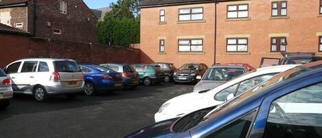 A parking lot with several cars parked in front of a brick building with multiple windows.