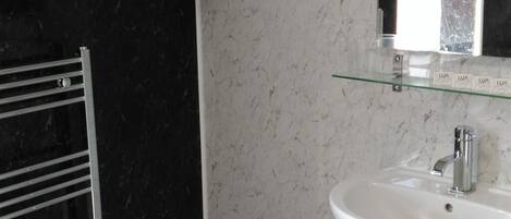 Une salle de bain avec un mur en marbre noir, un lavabo blanc surmonté d’une étagère en verre, et un porte-serviettes avec des serviettes pliées.
