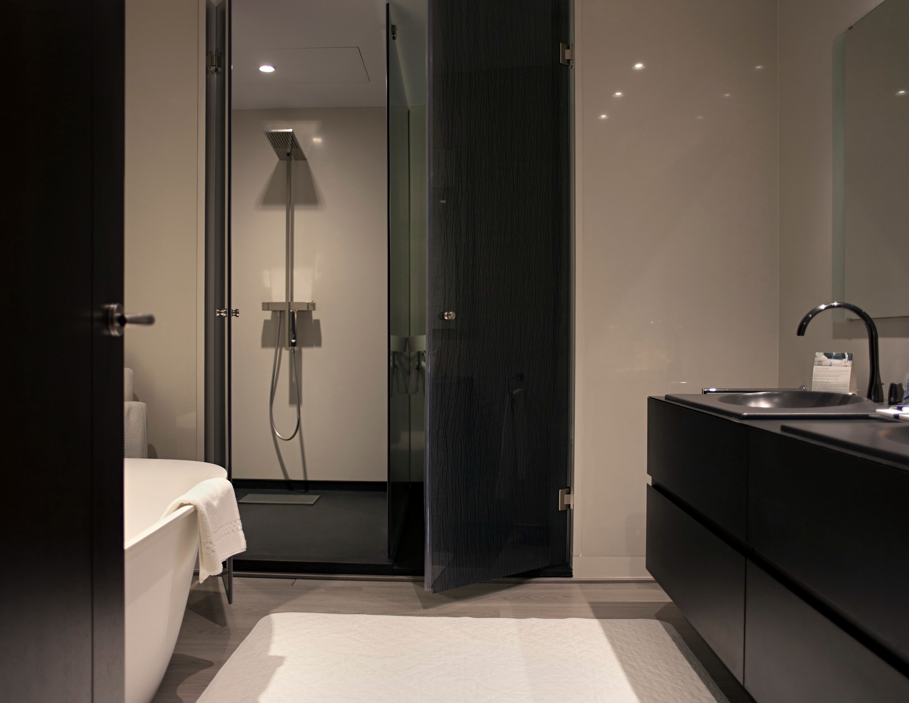 A modern bathroom with a walk-in shower, a large mirror, and a dark-toned vanity.