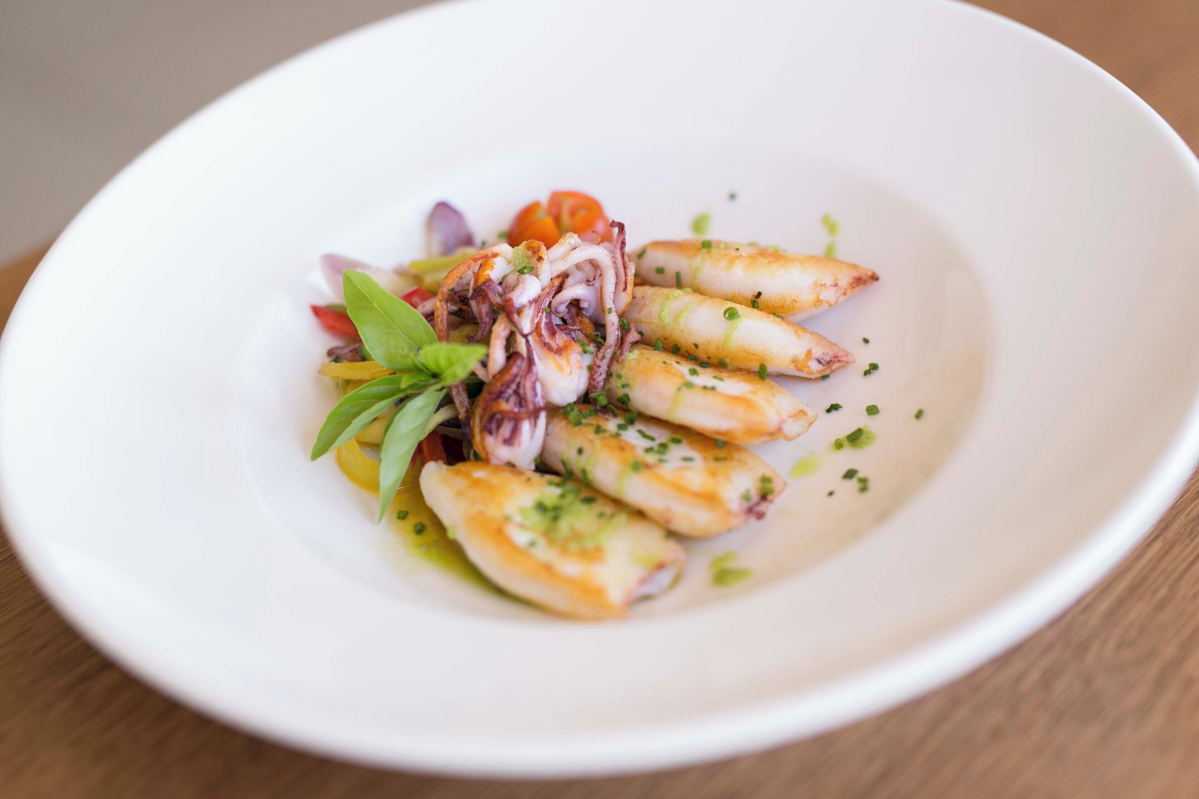 Un plato blanco con calamarres a la plancha, una ensalada pequeña y algunas hierbas.