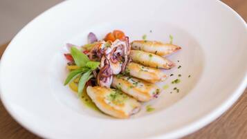 Un plato blanco con calamarres a la plancha, una ensalada pequeña y algunas hierbas.