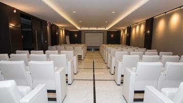 Une salle de conférence avec des rangées de chaises blanches, un grand écran à l’avant et un sol en marbre poli.