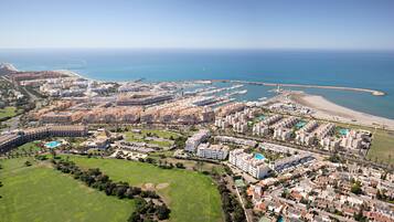 Vue aérienne d’une station balnéaire comprenant plusieurs bâtiments, un port de plaisance et une plage.