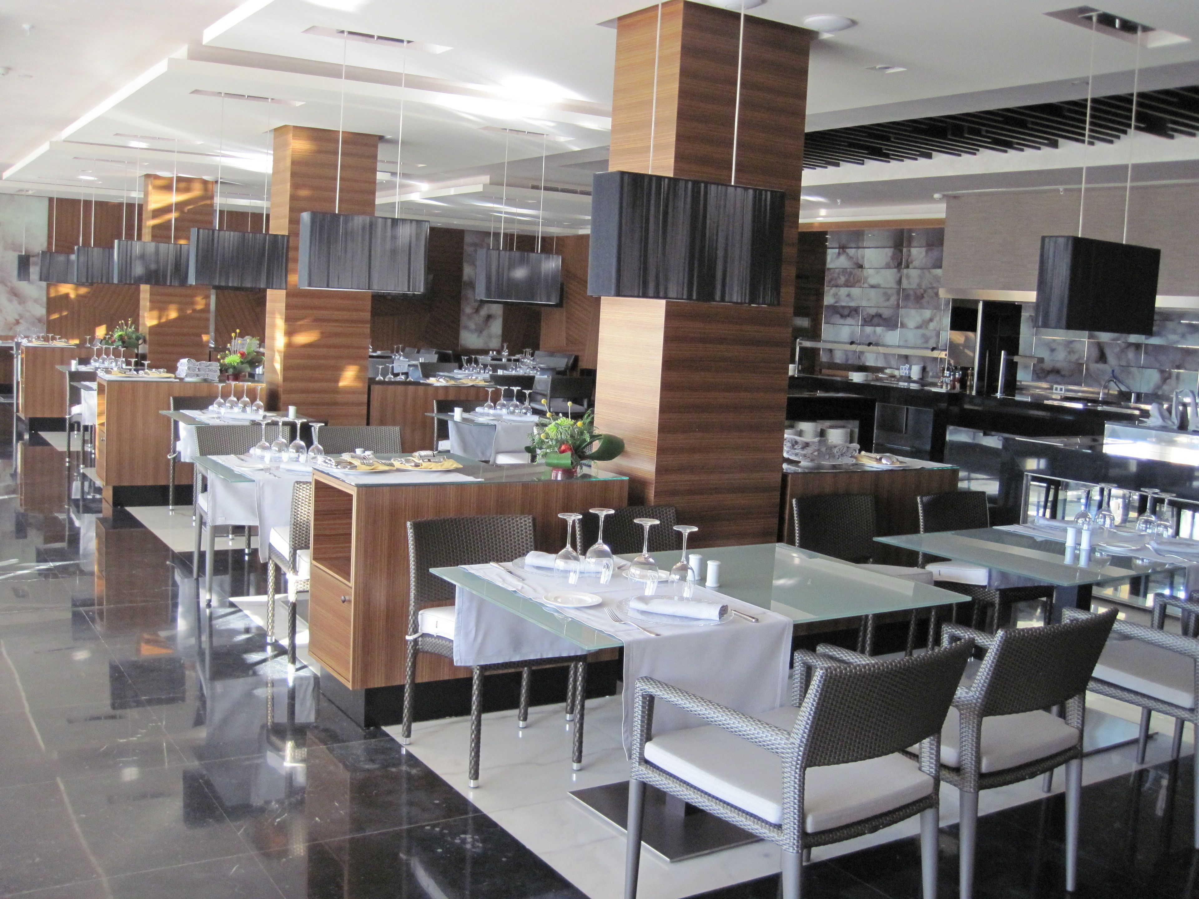 A modern restaurant with glass tables and chairs, wooden accents, and a clean, polished floor.