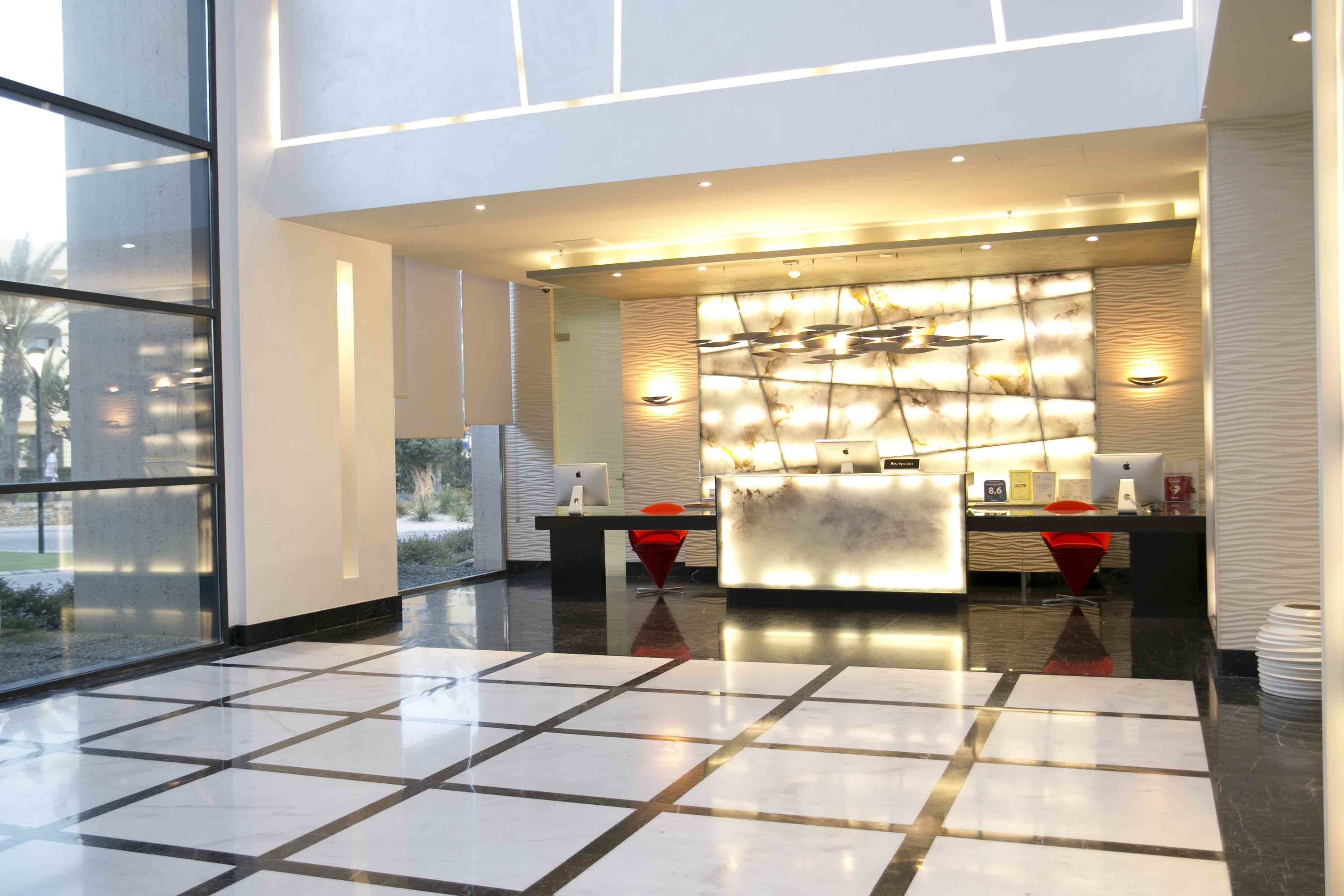Un área de recepción moderna con un muro de vidrio, un mostrador de recepción y una pared decorativa con iluminación.