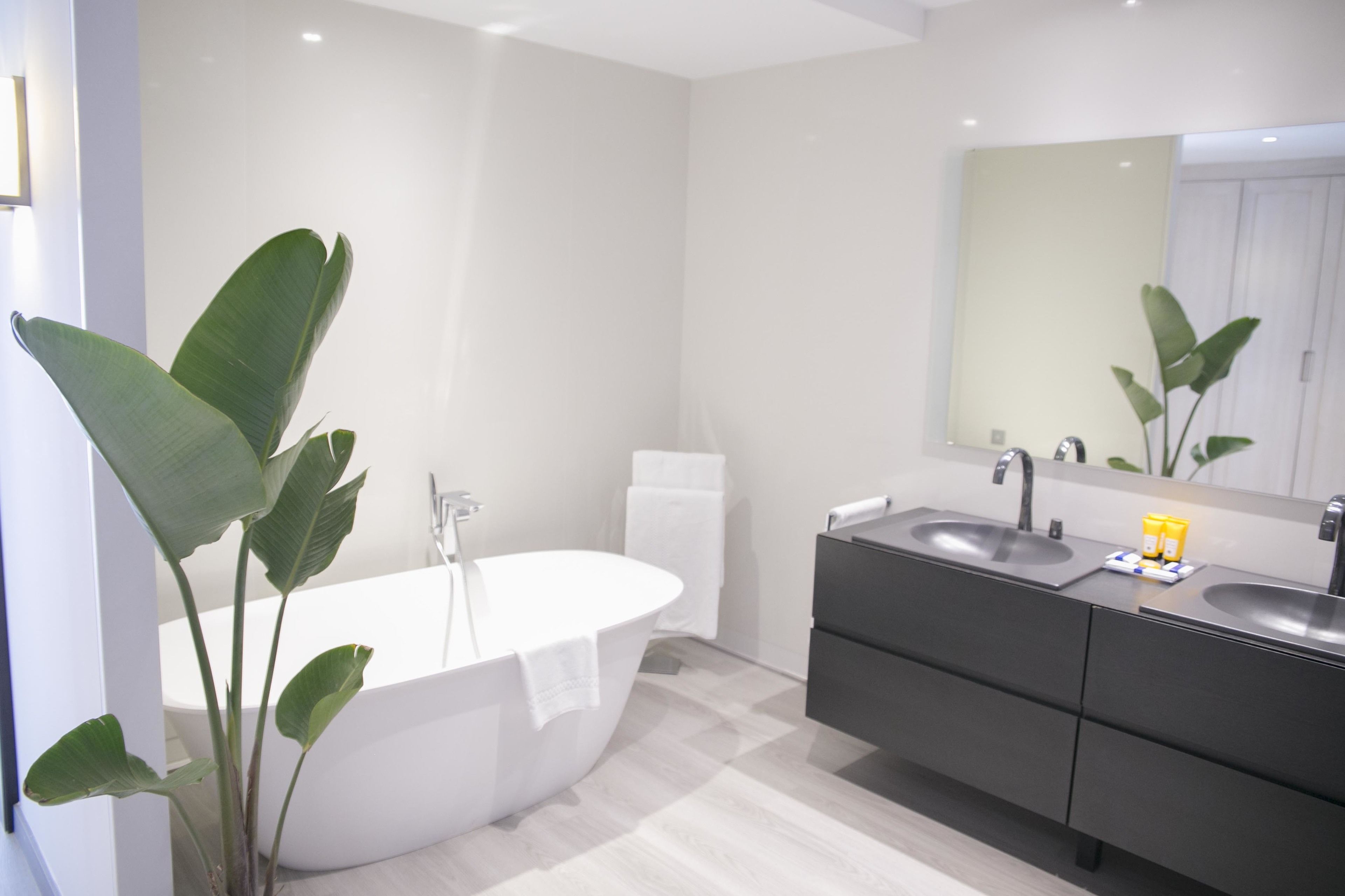 Un baño moderno con una bañera independiente, un tocador con dos lavabos y un espejo grande.