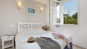 Ein Schlafzimmer mit einem Bett, einem Nachttisch, einem Fenster mit freier Aussicht und Wandleuchten.