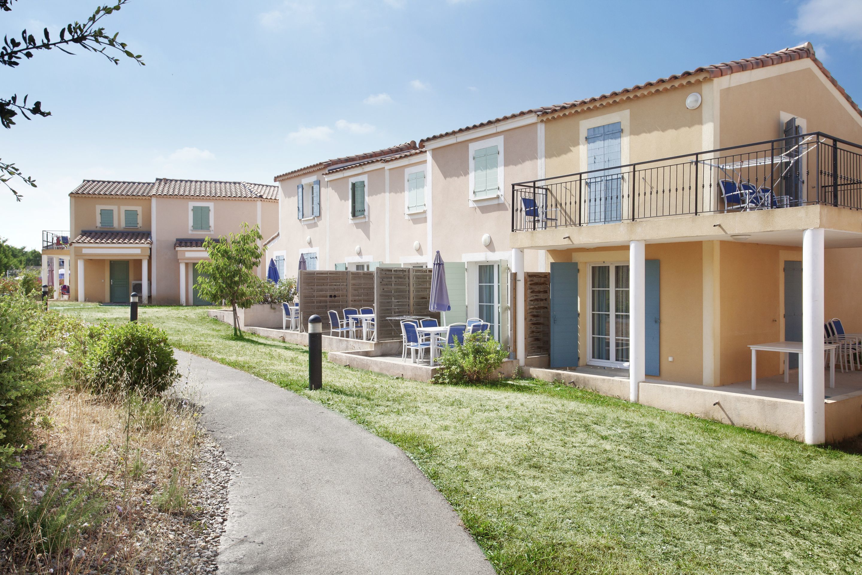 Un immeuble résidentiel doté d’un chemin pavé, d’un espace extérieur aménagé avec des sièges et d’un balcon avec des chaises.