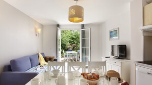 Eine moderne Küche mit weißen Geräten, einem für das Frühstück gedeckten Esstisch und Blick auf den Garten durch eine offene Tür.