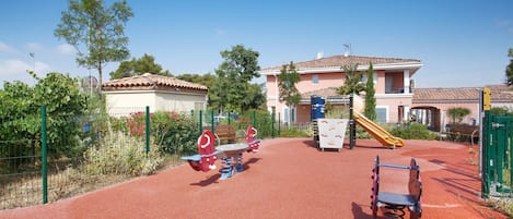 Une aire de jeux avec des balançoires, un toboggan et une structure d’escalade.