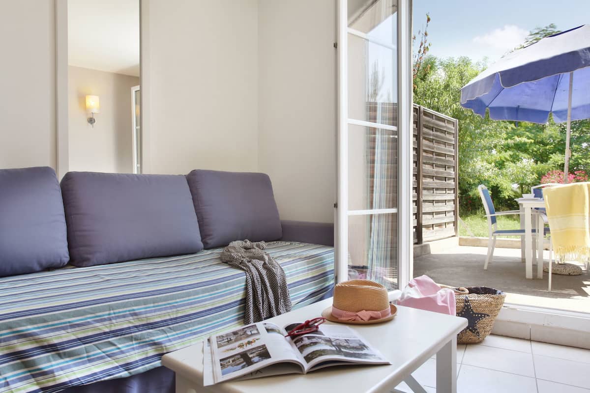 Una habitación acogedora con un sofá a rayas, una mesa con una revista, un sombrero de paja y una cesta de mimbre.