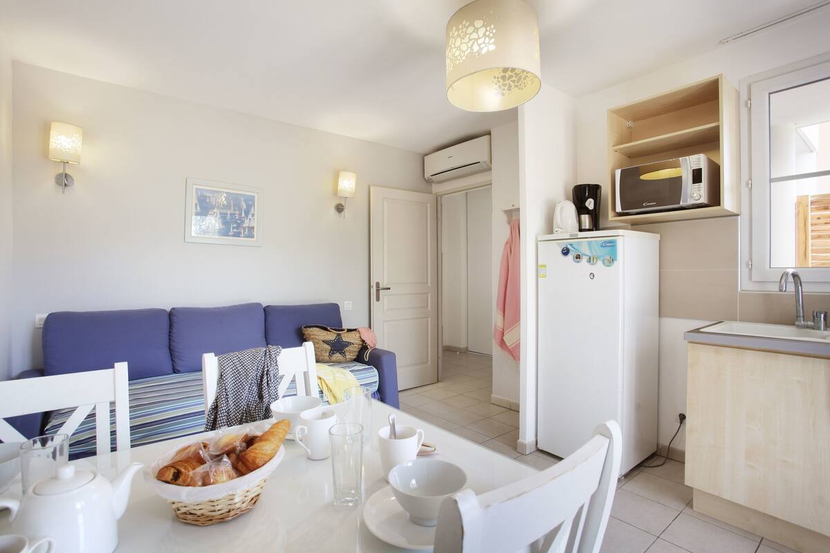Una cocina moderna con electrodomésticos blancos, una mesa de comedor con alimentos para el desayuno y un sofá azul en la sala.