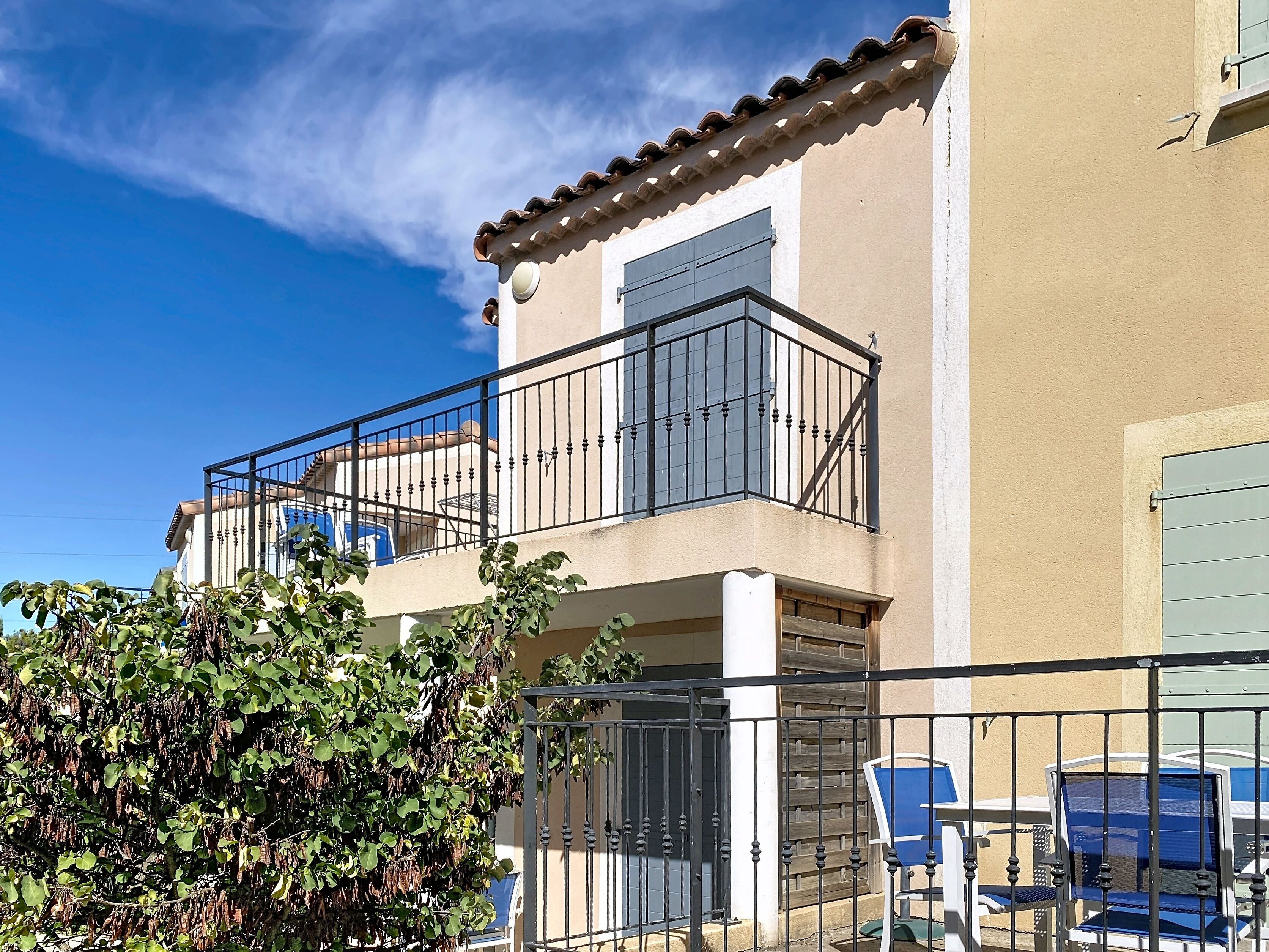 Ein zweistöckiges Gebäude mit Balkon, Tor und Gartenmöbeln.
