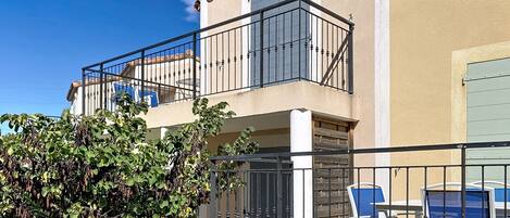 Ein zweistöckiges Gebäude mit Balkon, Tor und Gartenmöbeln.