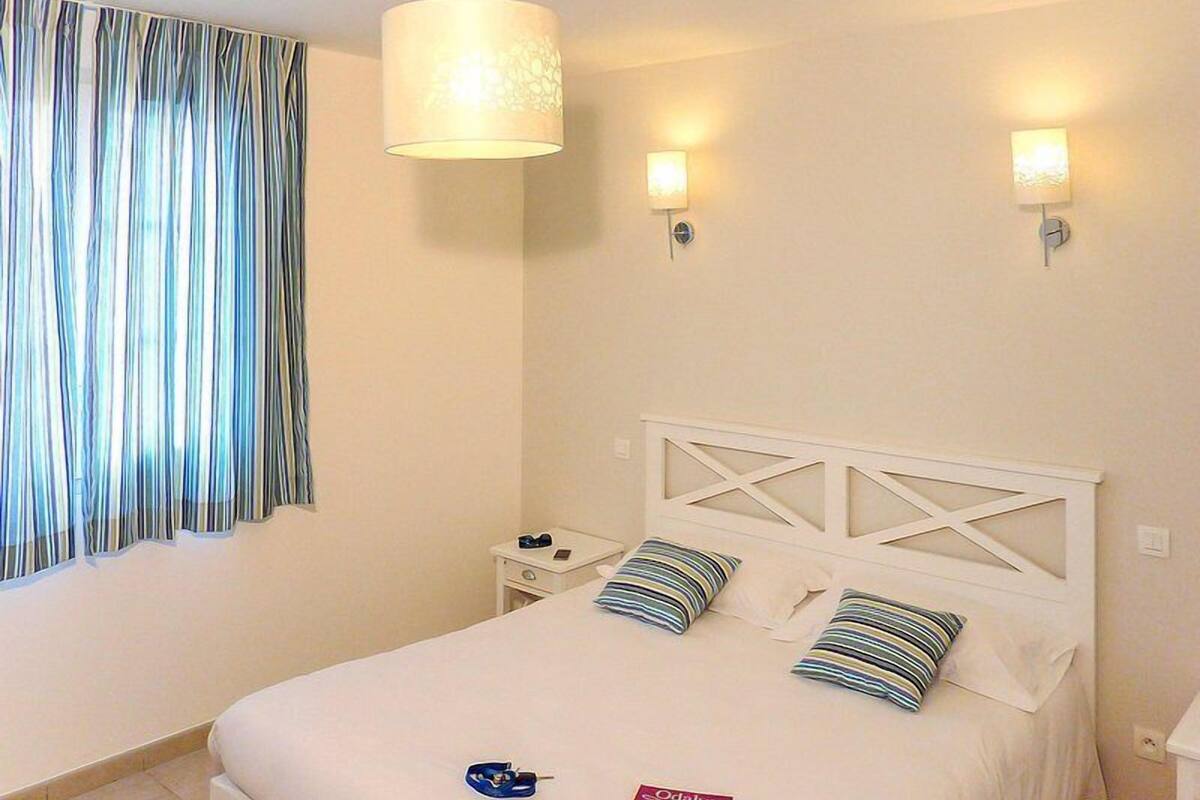 Un dormitorio con una cama, dos lámparas de noche, una mesita de noche y un ventanal con cortinas.