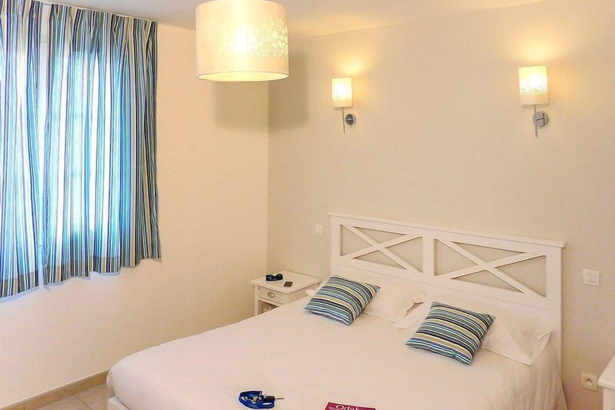 A hotel room with a bed, two bedside lamps, a nightstand, and a curtain.