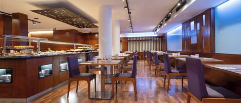 Um restaurante moderno com piso de madeira, área de buffet e sala de jantar com mesas e cadeiras.