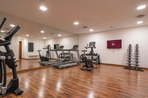 Una palestra con diverse attrezzature per esercizi, tra cui tapis roulant e cyclette, e un televisore a parete.