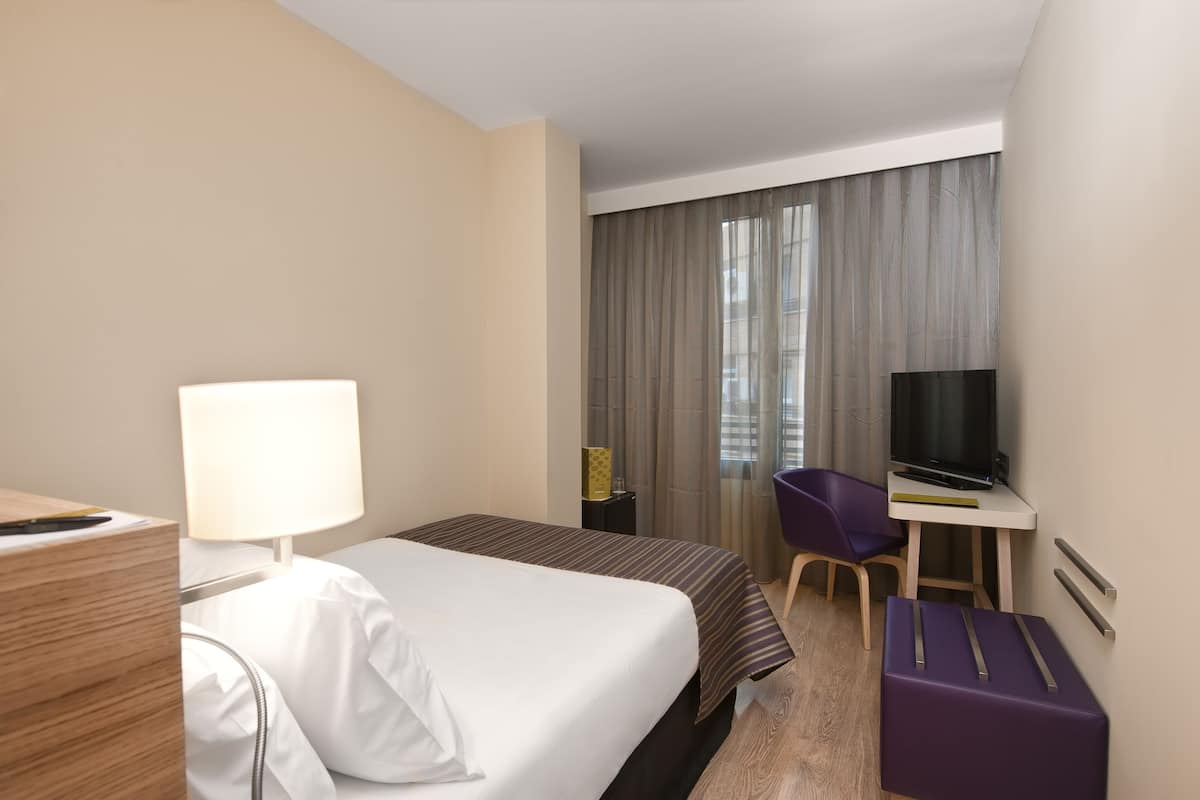 Una habitación de hotel con cama, escritorio con televisor, silla y maleta.