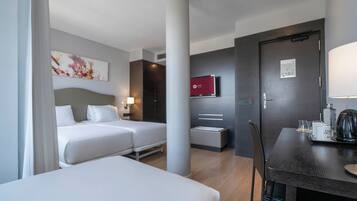 Una habitación de hotel con dos camas, un escritorio con cafetera y un televisor en la pared.