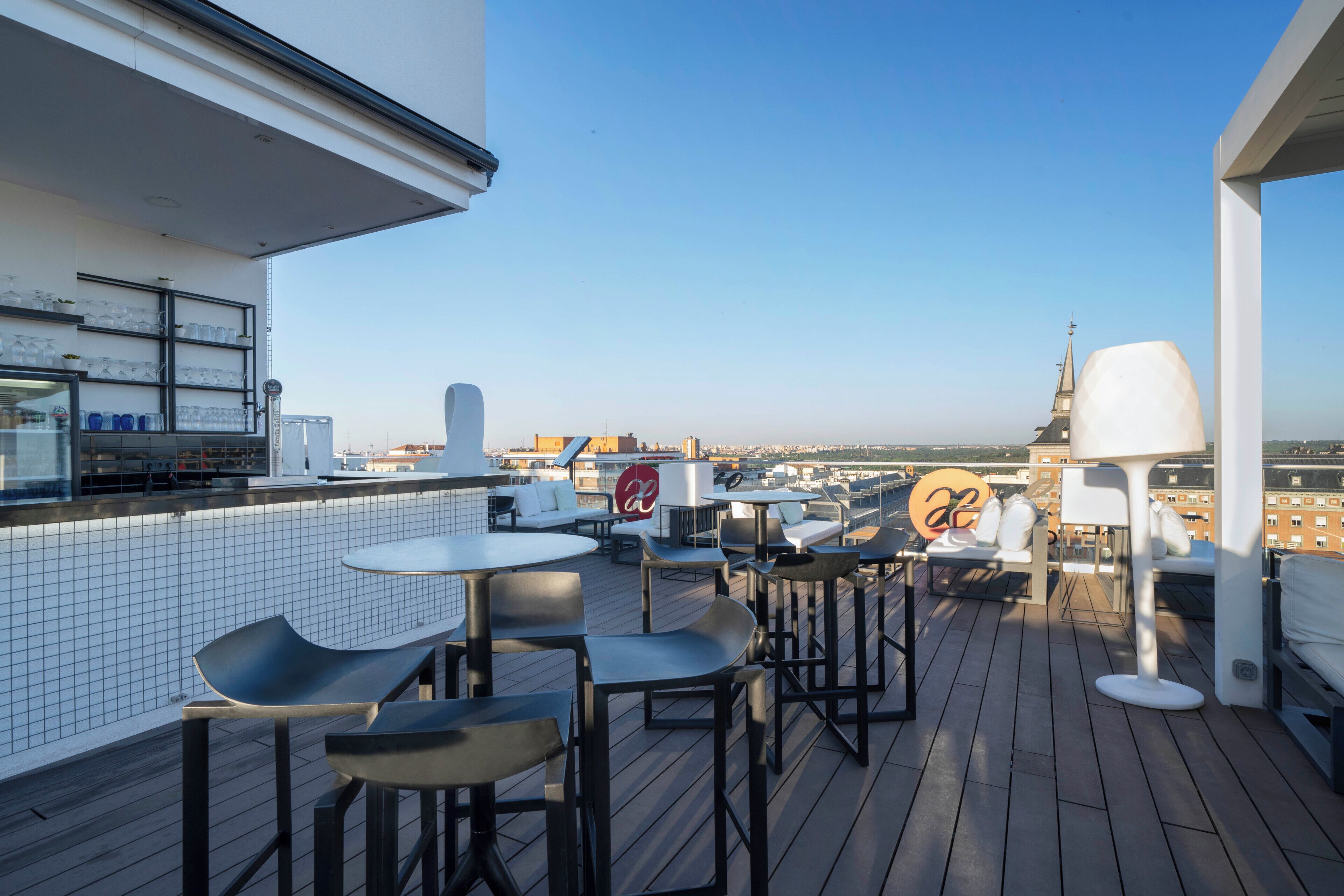 A rooftop terrace with tables, chairs, and a view of the cityscape.
