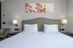 Una camera d'albergo con un letto grande, due comodini con lampade, una sedia e un'opera d'arte appesa al muro.