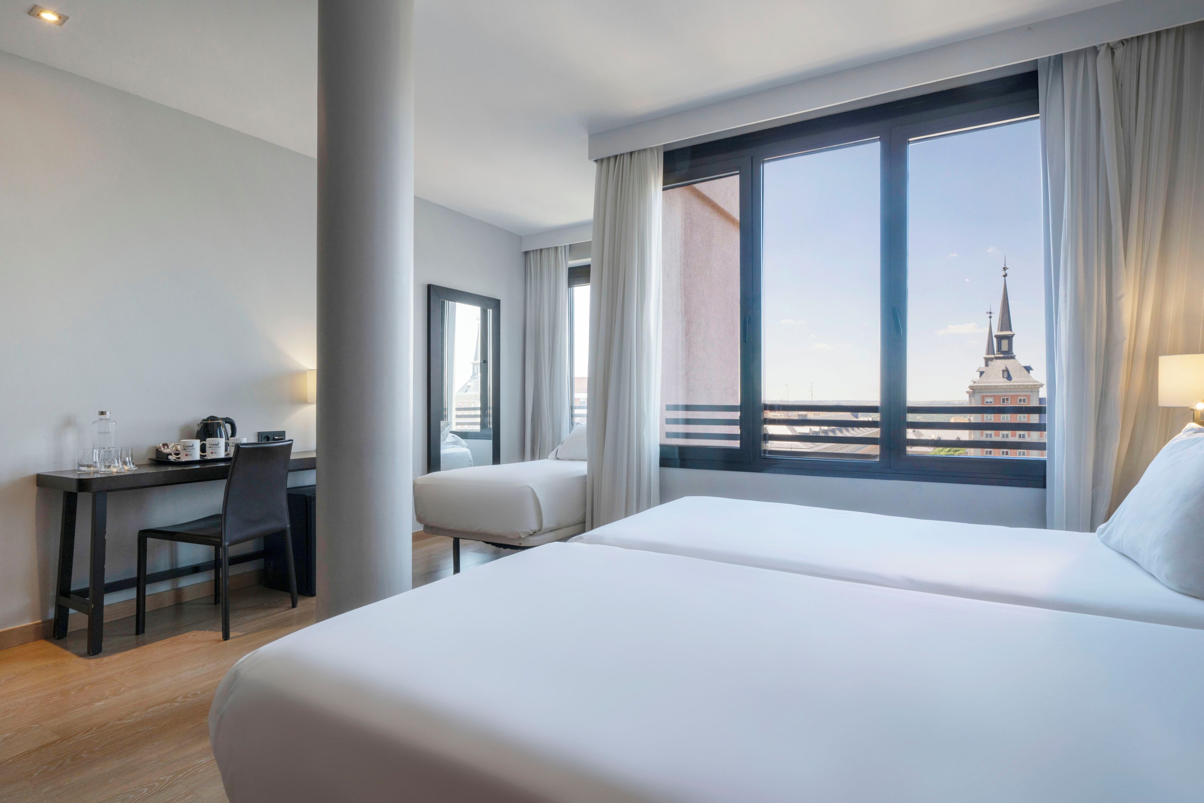 Habitación de hotel con cama, escritorio y silla. Se ve un edificio desde la ventana.