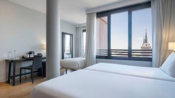 Habitación de hotel con cama, escritorio y silla. Se ve un edificio desde la ventana.