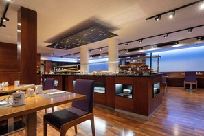 A modern breakfast bar with a variety of food options, a seating area with tables and chairs, and a large screen displaying a presentation. - Hotel Exe Moncloa (Madrid)