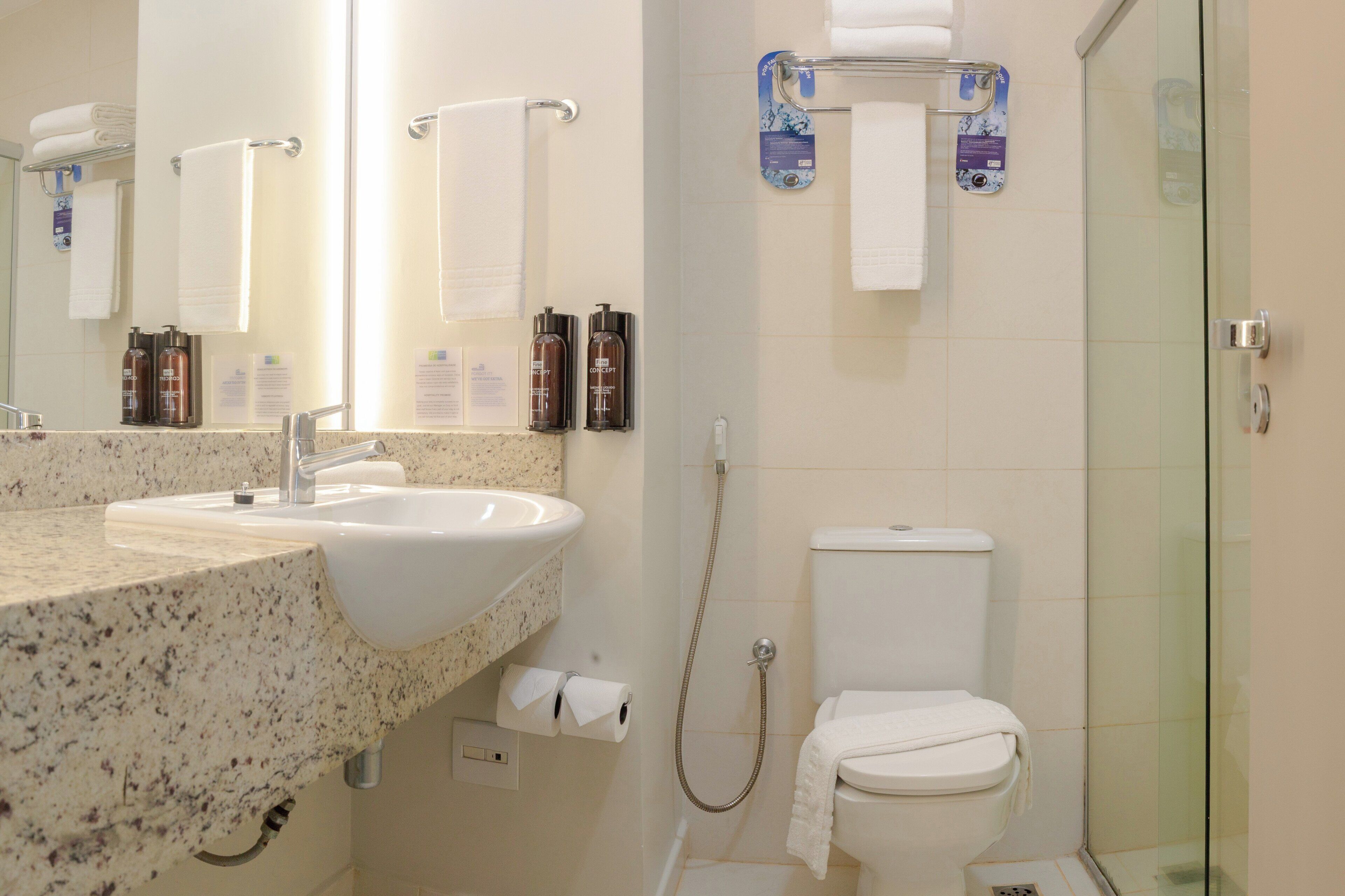 Un baño con lavamanos, espejo, toallero, inodoro y ducha.
