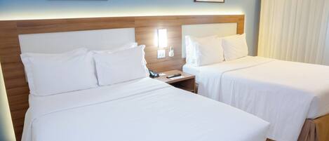 A hotel room with two beds, a wooden headboard, a nightstand with a phone, and framed pictures on the wall.