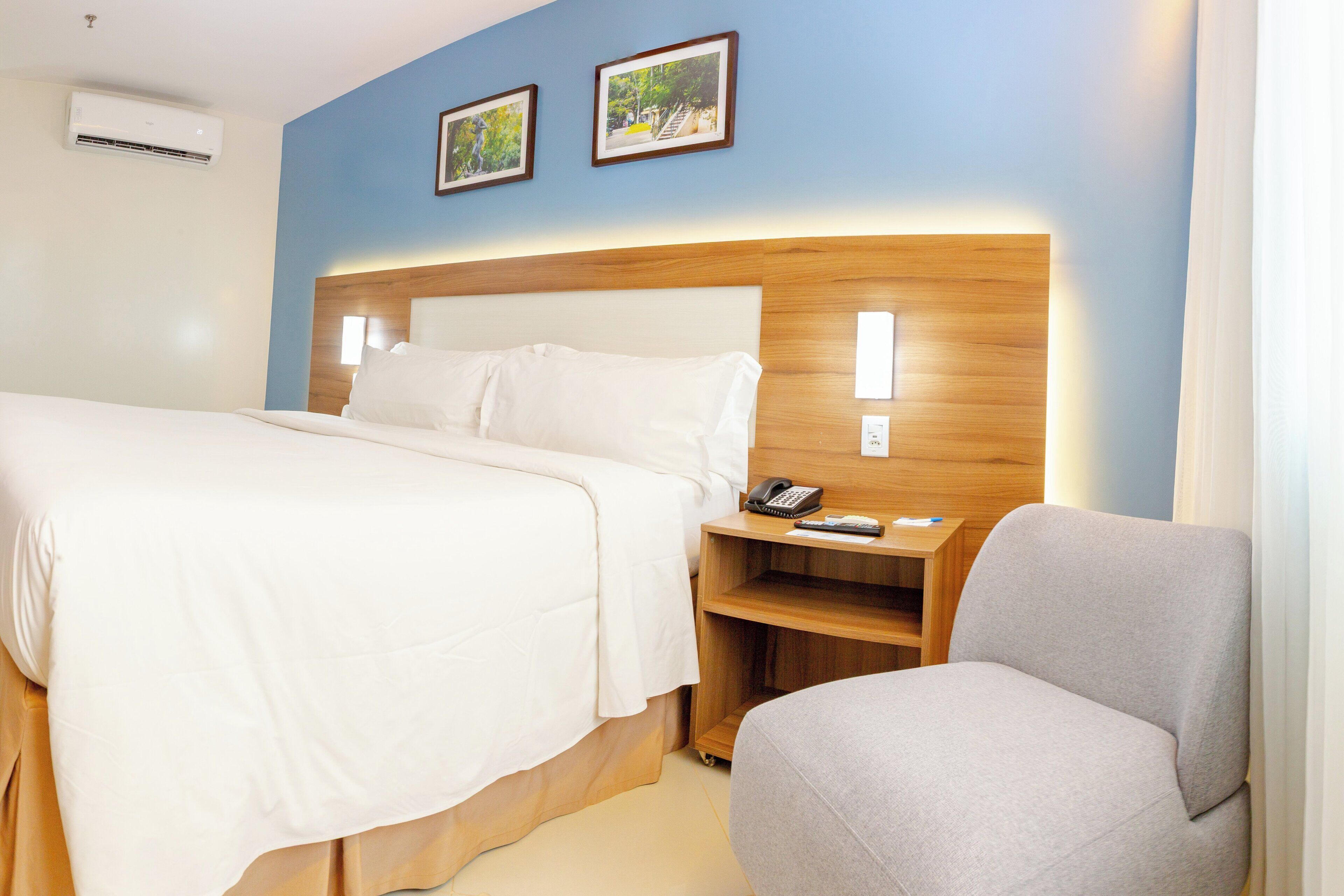 Ein Hotelzimmer mit Bett, Nachttisch, Stuhl und zwei gerahmten Bildern an der Wand.
