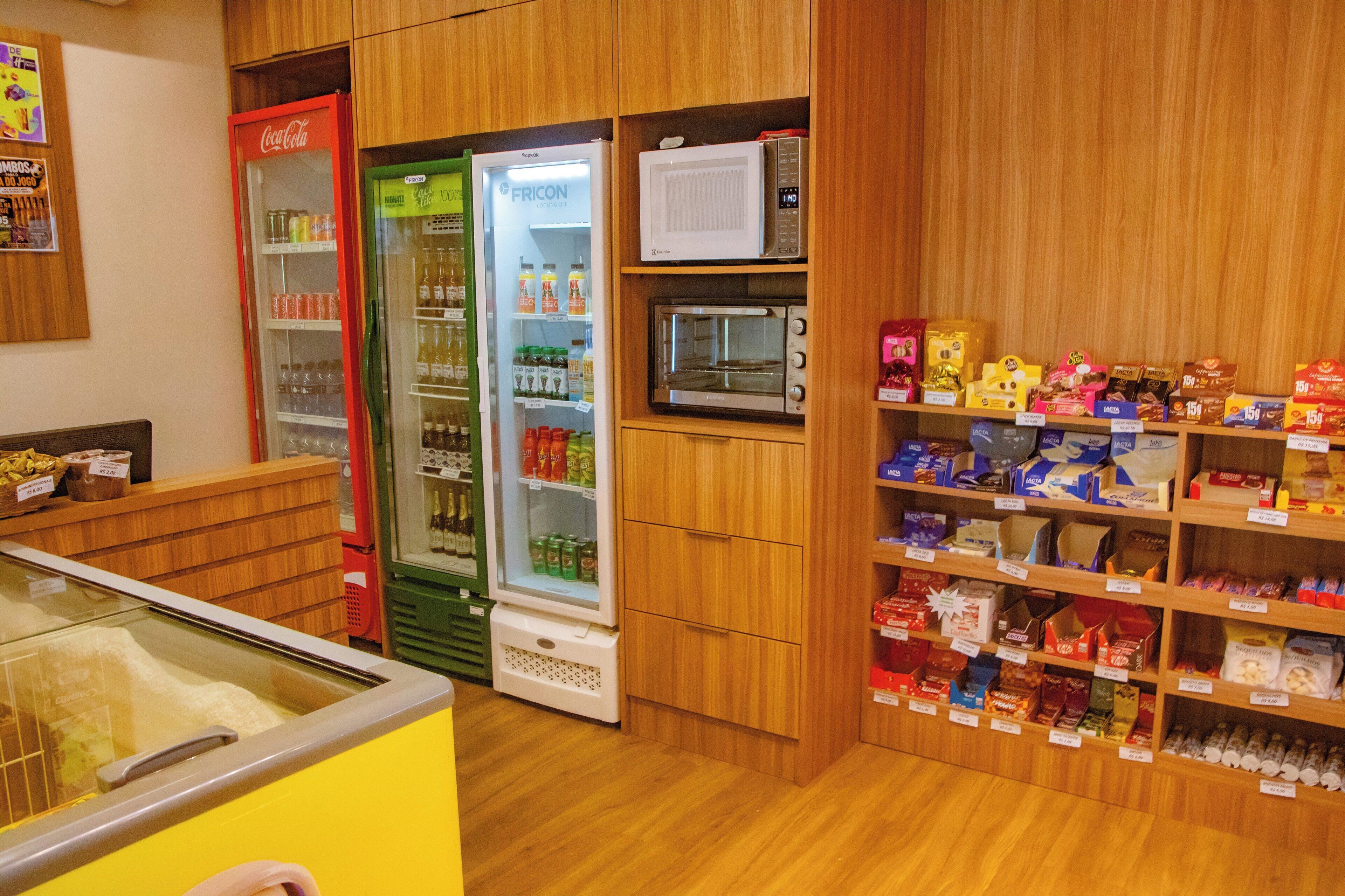 Interior de una tienda con un refrigerador, microondas y estantes repletos de diferentes productos.