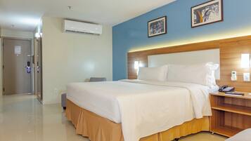 Habitación de hotel con una cama grande, una mesita de noche con teléfono y control remoto, aire acondicionado montado en la pared y una puerta con un cartel.
