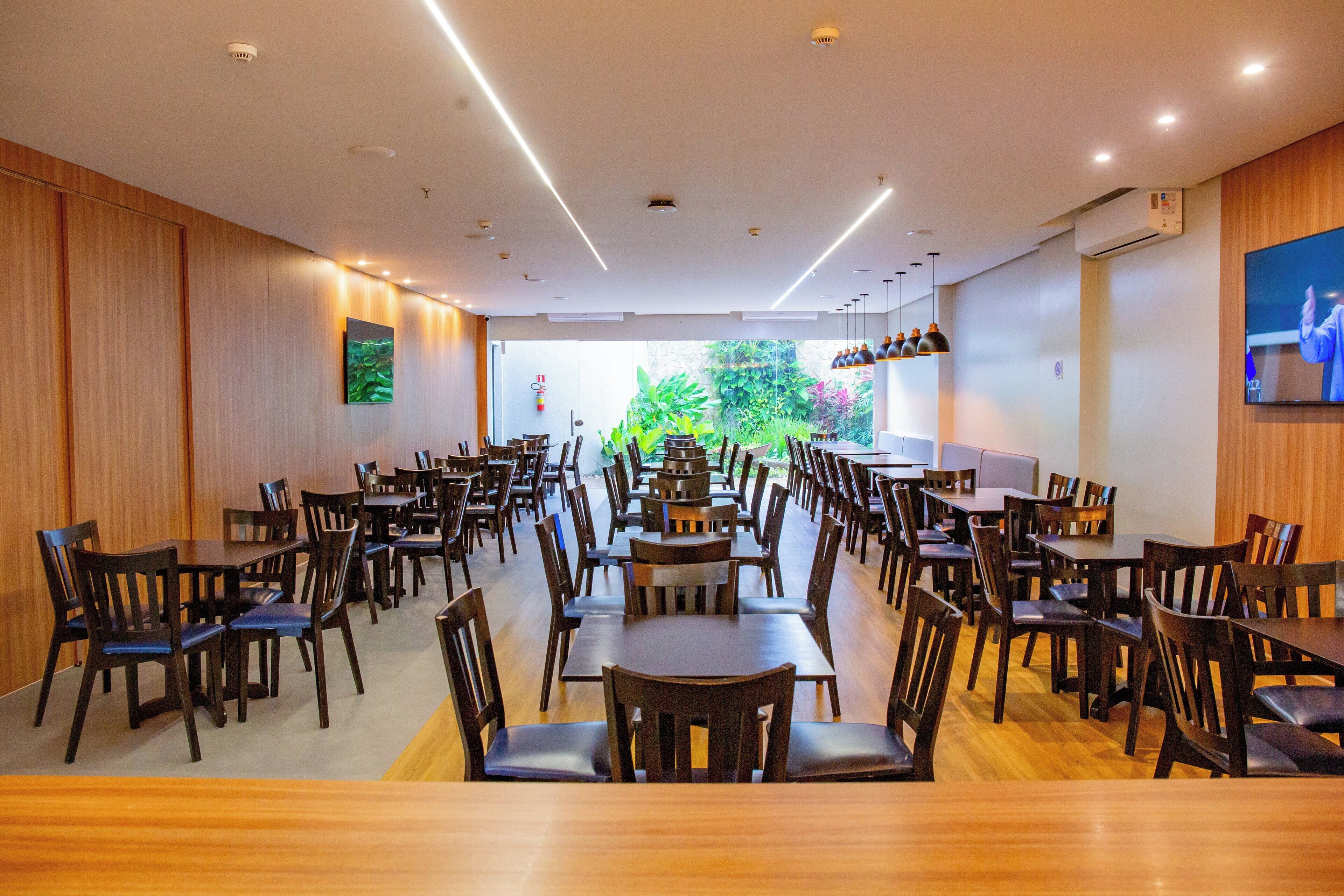 Un vaste espace de restauration intérieur, doté de nombreuses tables et chaises, de murs en bois et offrant une vue sur la verdure environnante.