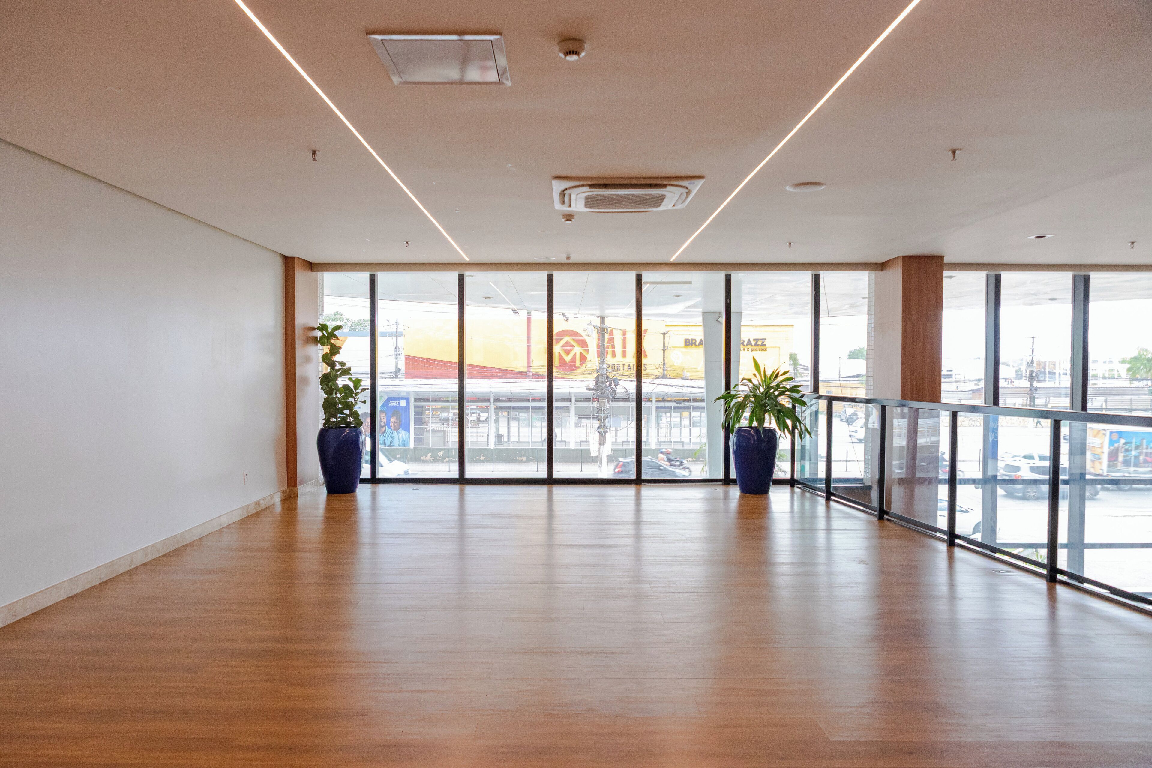 A spacious room with large windows, wooden flooring, and two potted plants.