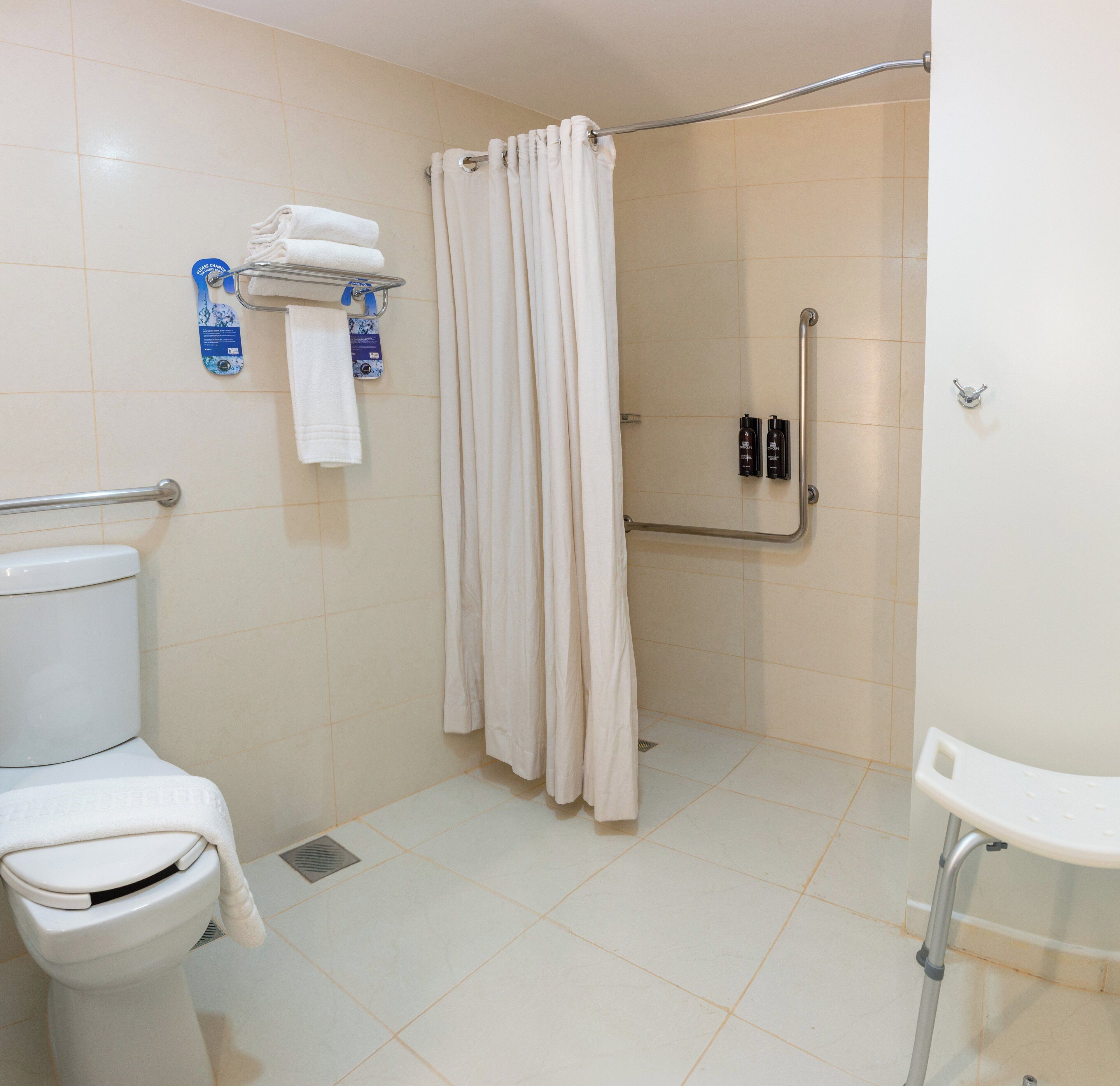 Un baño con inodoro, ducha con barra de apoyo y lavamanos.