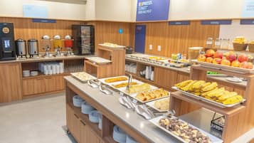 Buffet com diversas estações de comida, incluindo frutas, cereais e pratos quentes.