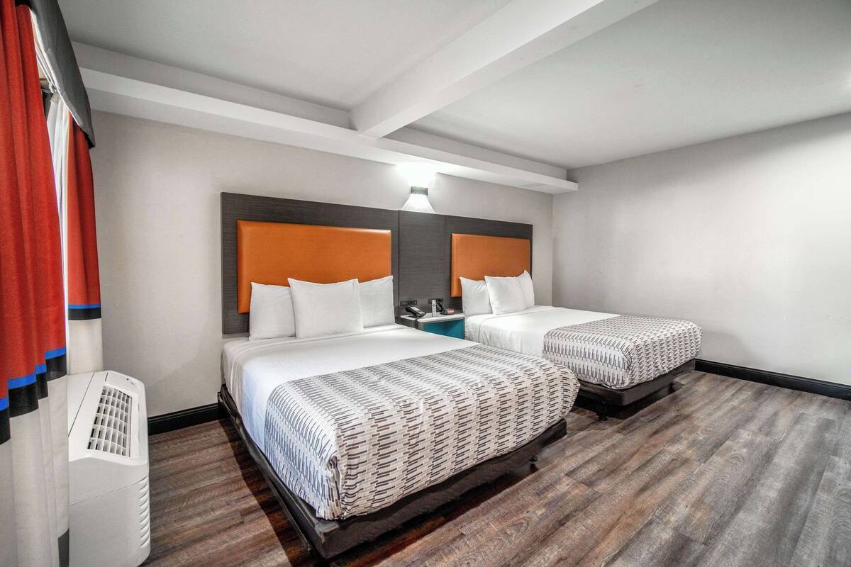A hotel room with two beds, a nightstand, a lamp, and a heater.
