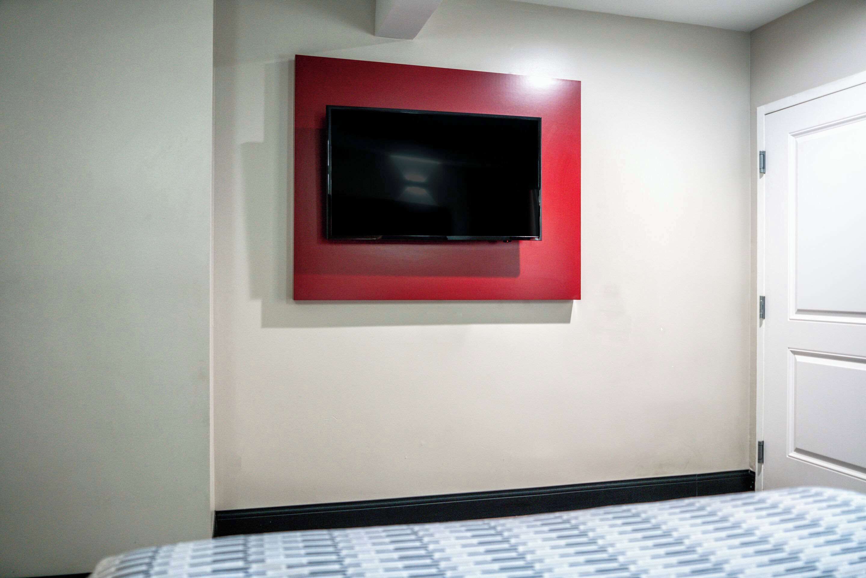 Una habitación de hotel con una cama, un televisor montado sobre un panel rojo y una puerta blanca.