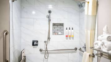 Un espace douche moderne doté d’une porte en verre, d’une barre d’appui et d’un porte-serviettes avec des serviettes pliées.